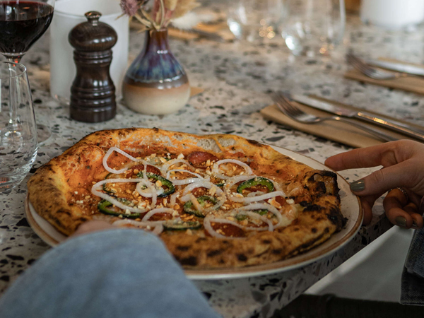 Gäst äter pepperonipizza med ett glas rött på Corner