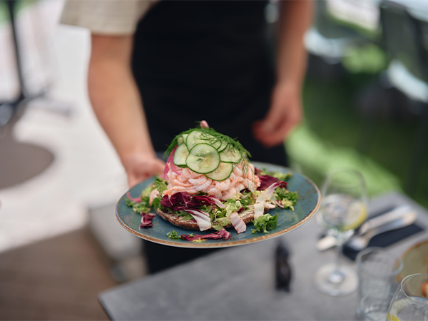 Servitör serverar en räkmacka på Corners uteservering på Gothia Towers